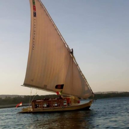 A traditional sailboat with a large sail gliding on the Nile River at sunset.