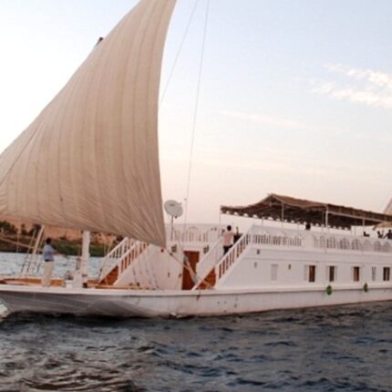 A white sailboat with two large sails cruising on the Nile River at sunset.