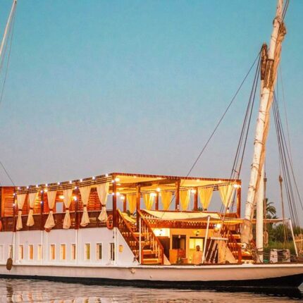 A beautifully lit Dahabiya boat with two decks, sailing on calm waters at dusk.