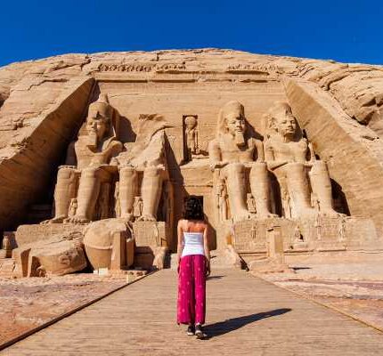 Woman in red pants walking towards the massive statues at the entrance of the Abu Simbel temples.