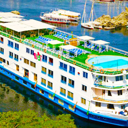 A Nile River cruise ship with a rooftop pool and lounge chairs, docked by the river.