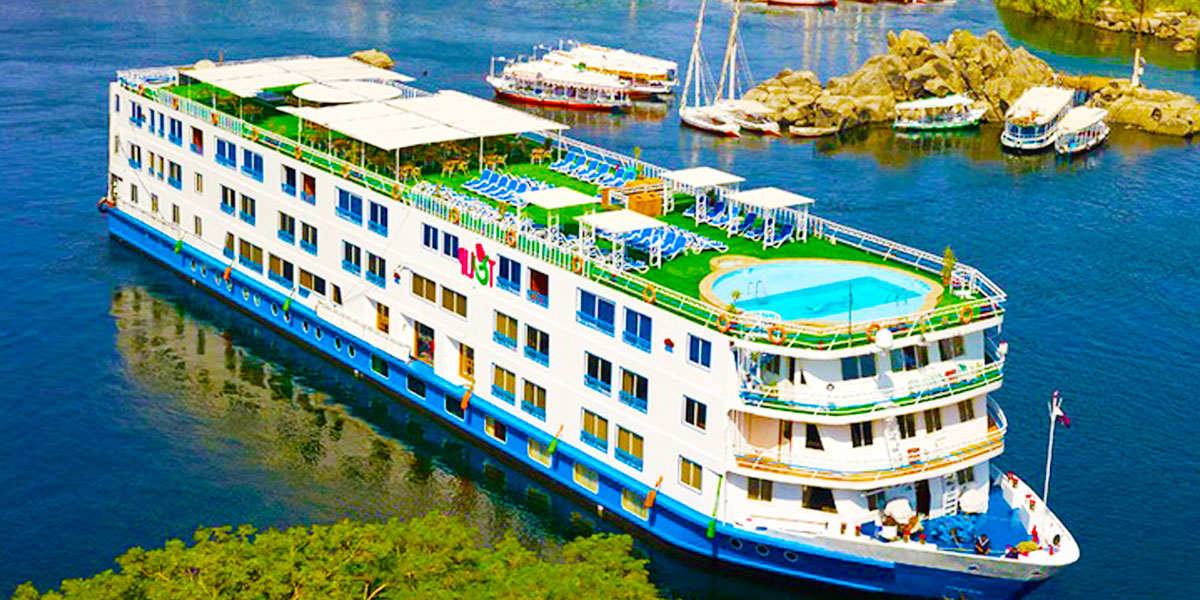 A Nile River cruise ship with a rooftop pool and lounge chairs, docked by the river.