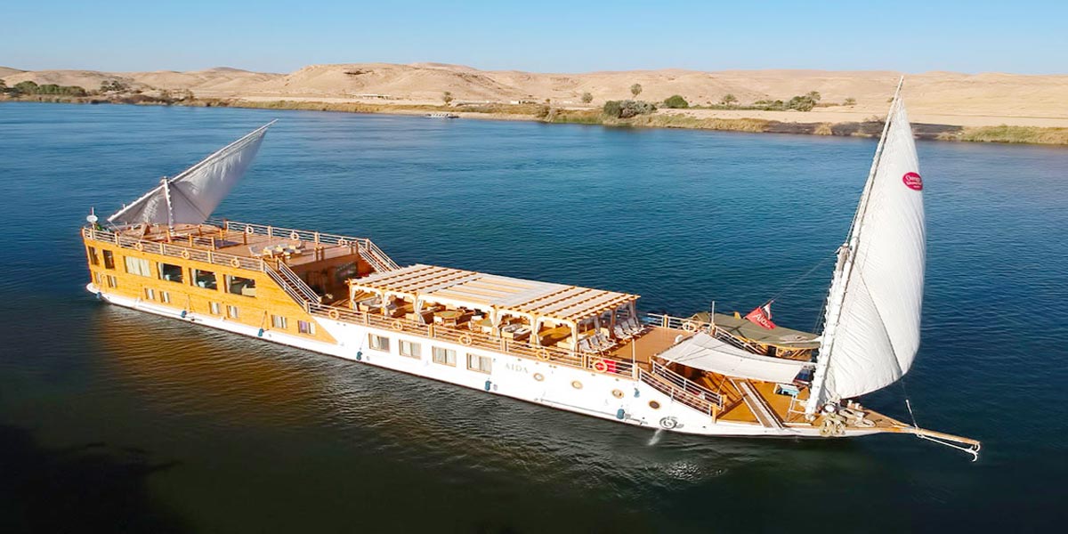 Aida Dahabiya Nile cruise boat sailing on a calm river with a scenic desert background.