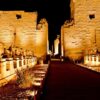 Night view of the illuminated Karnak Temple entrance with rows of sphinx statues.