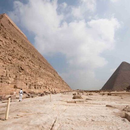 Two pyramids at Giza against a cloudy sky with a person walking near the base.