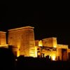 Philae Temple illuminated at night with golden lights highlighting the hieroglyphics and architecture.